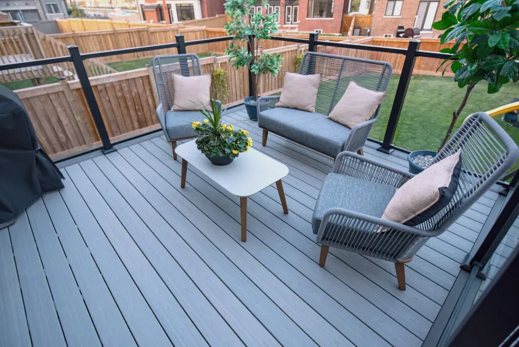 Grey backyard deck with lounge seating, visible board grain and black-framed glass railings