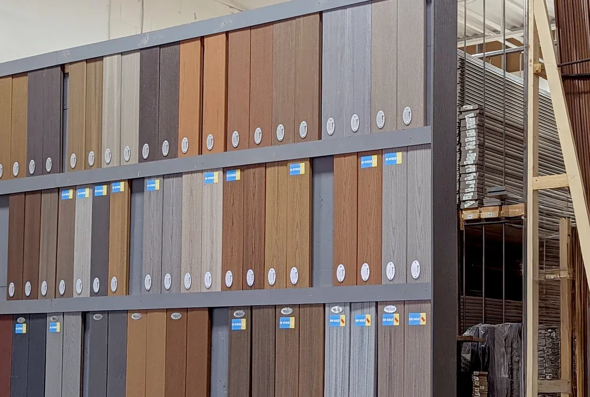 Real decking board samples in brown, grey and wood tones on a Composite Deck Shop display wall