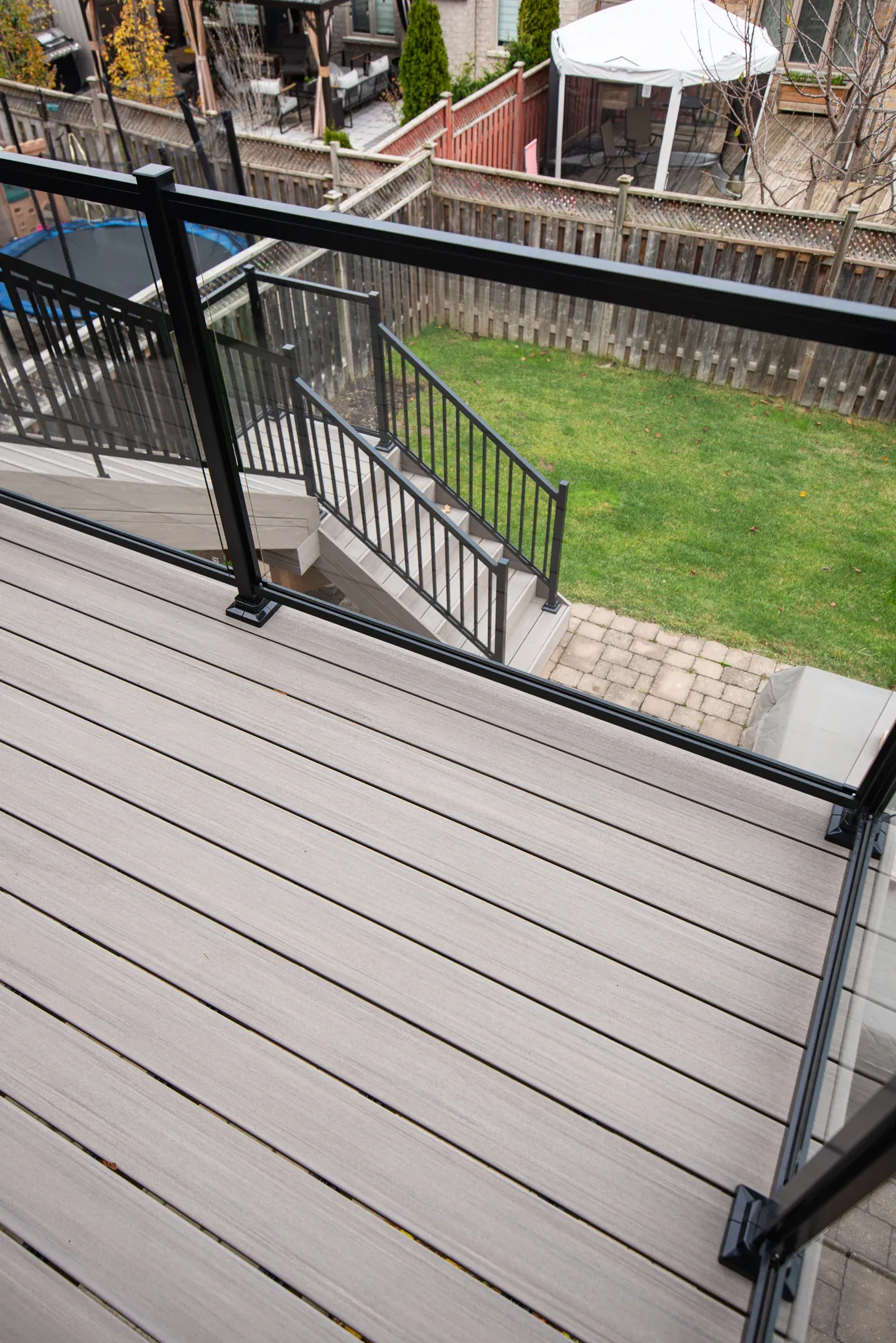 Black guard posts with glass infill beside grey deck boards and a descending picket stair guard.