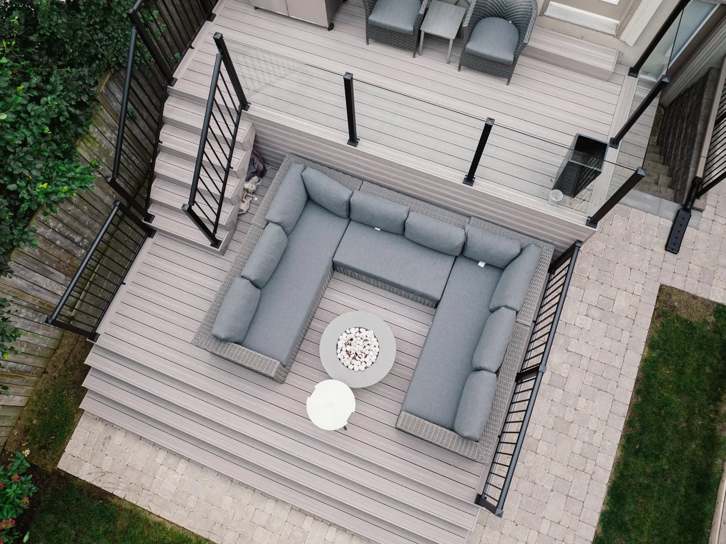 Overhead view of a finished two-level composite deck with picture-frame borders, wide stairs, glass panels and black picket railings