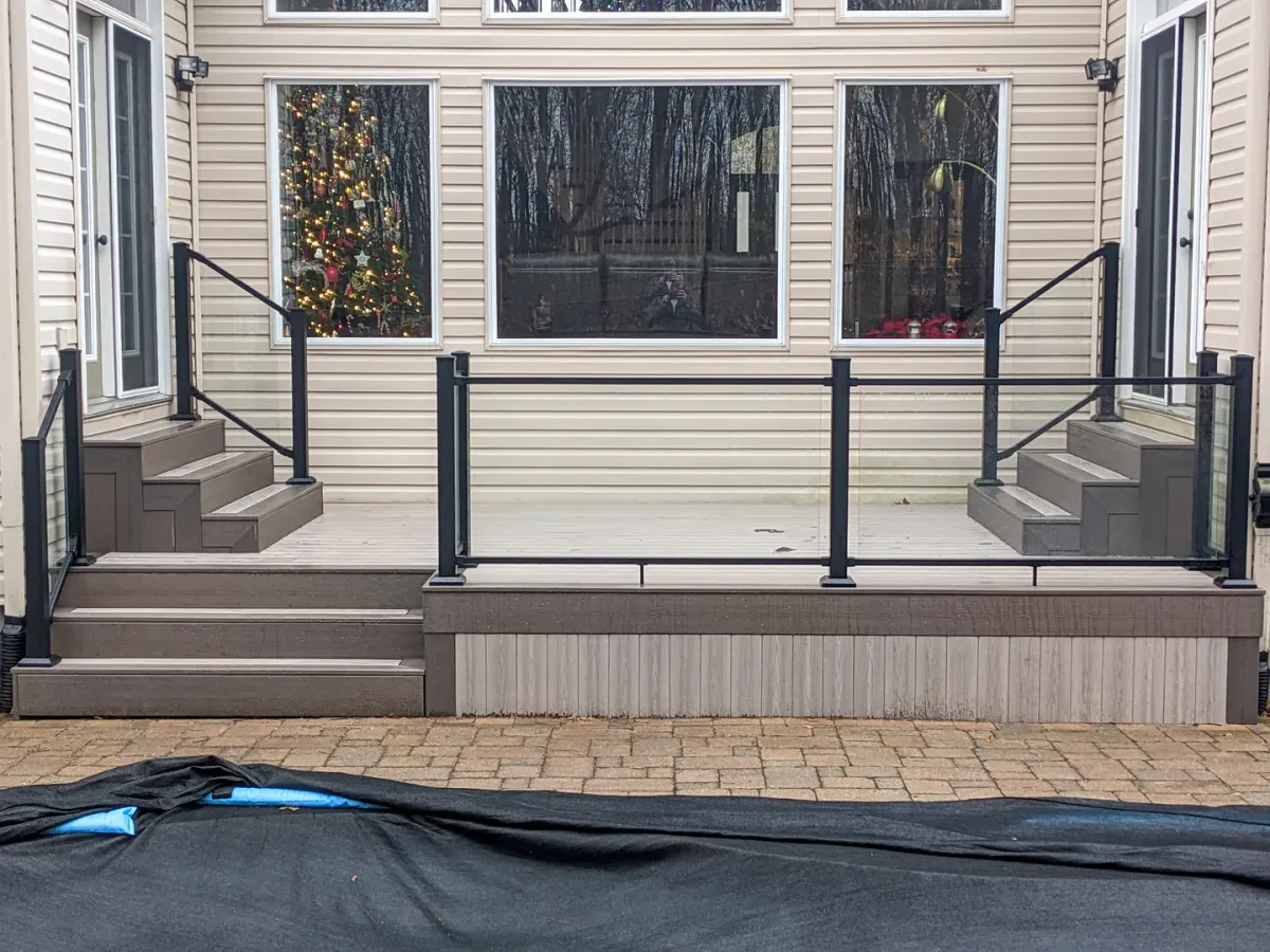 Clear glass railing panels and black posts enclosing a low deck with steps at both ends