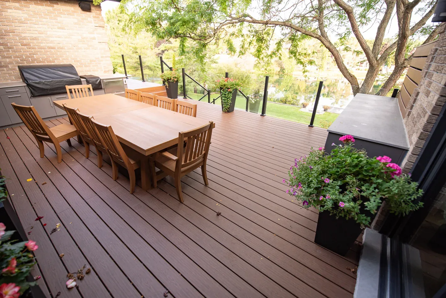 Brown Trex deck with a dining table, barbecue, wide board surface and glass railing
